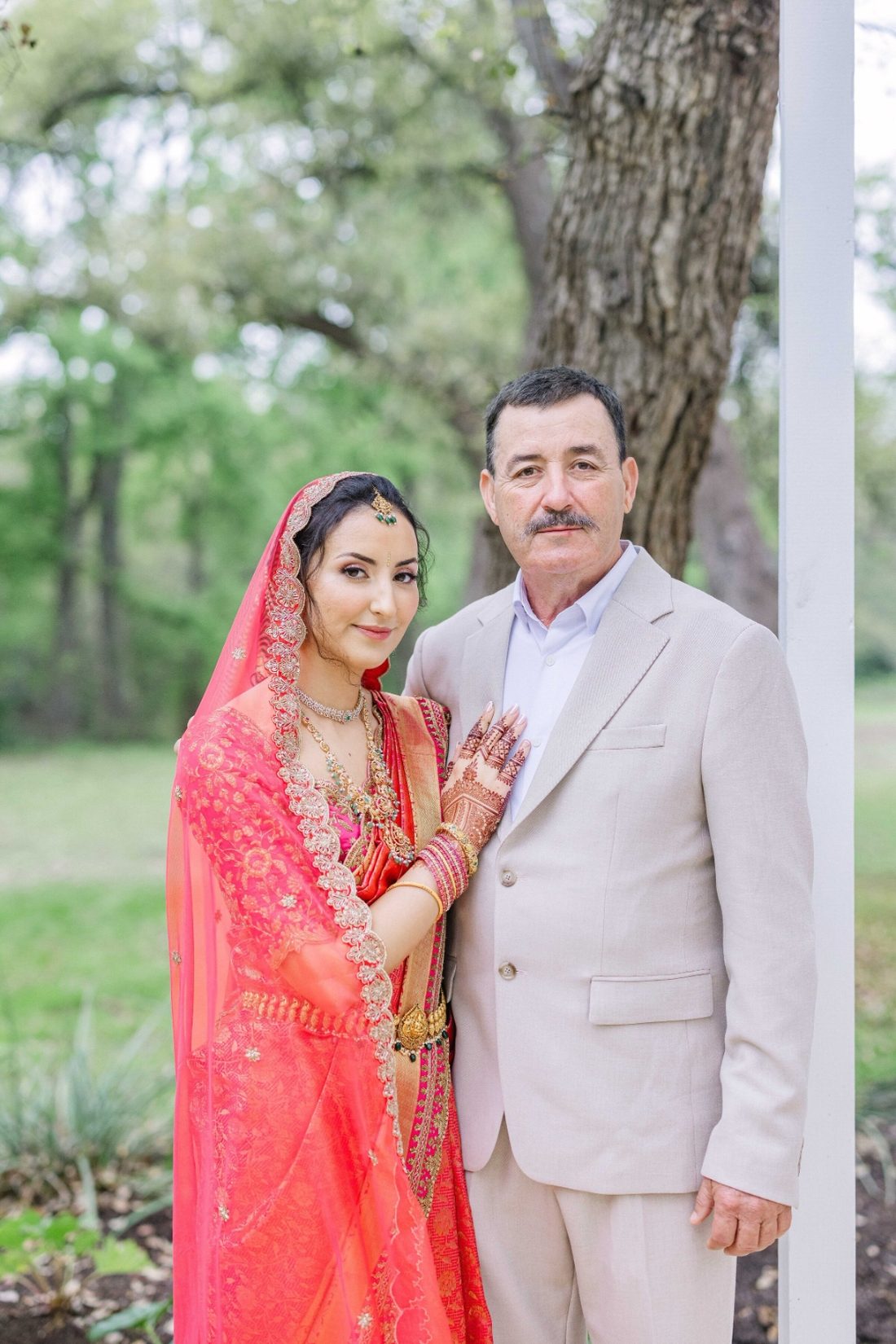 Bride in coral and gold attire standing beside her father for a tender portrait