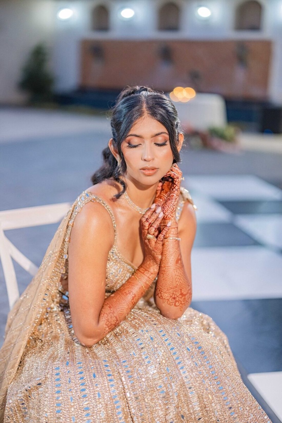 Bride in gold lehenga resting her mehndi-adorned hands beneath her chin