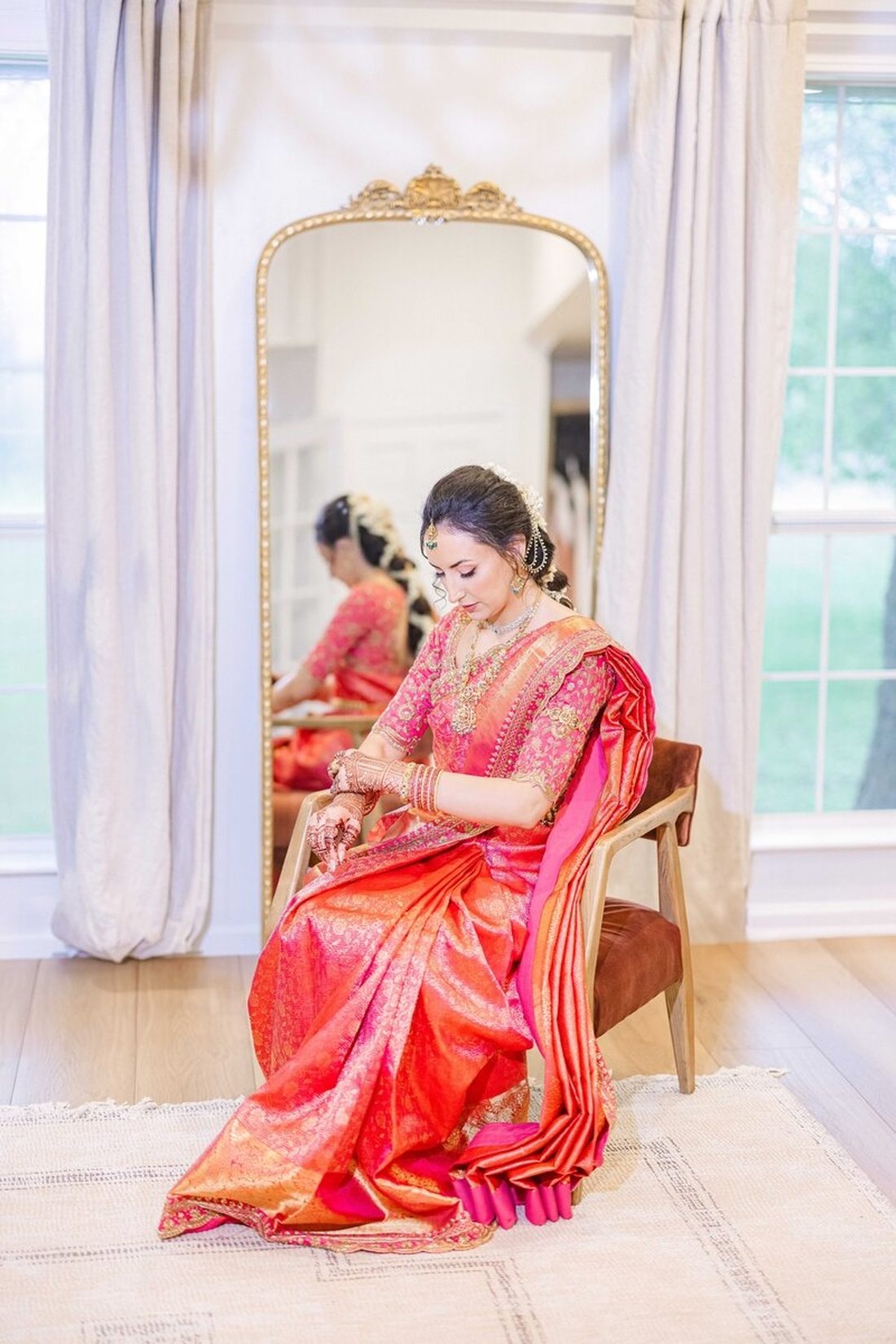 Bride seated before an ornate mirror adjusting bangles in pink and gold silks