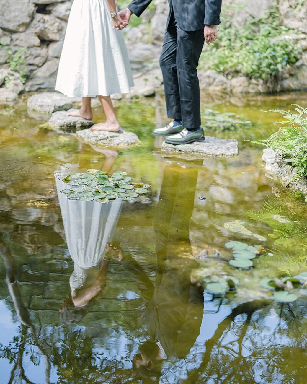 Couple hands joined over still pond with lily pads