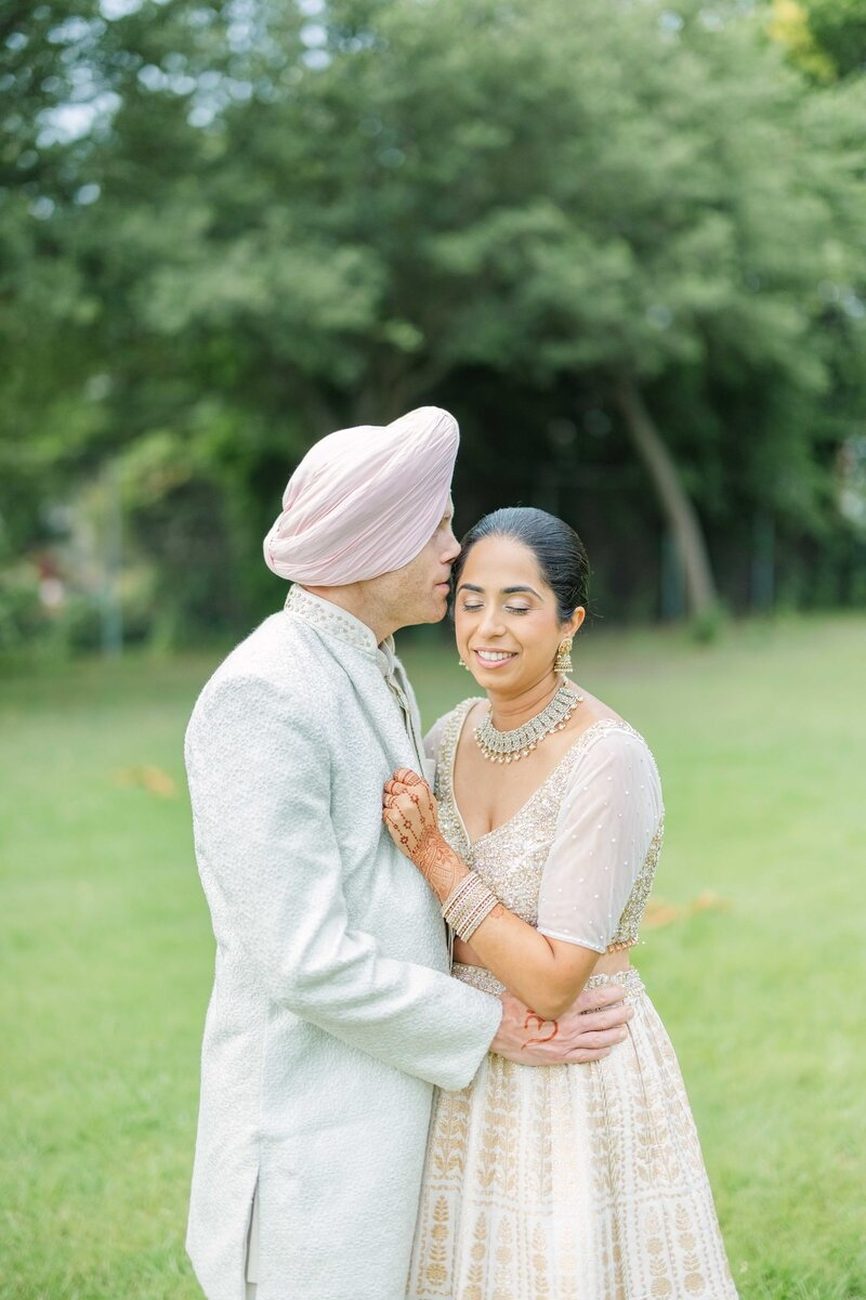 Parents embracing bride in coral saree under trees