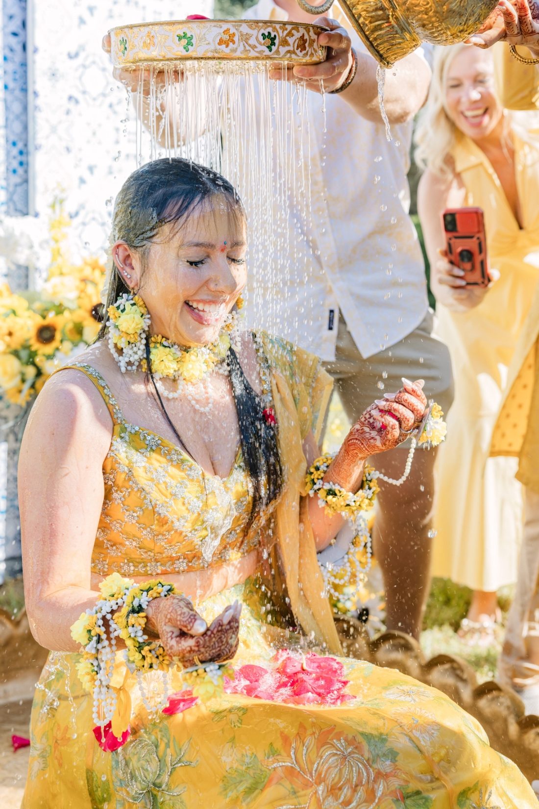 Bride laughing as turmeric-tinted water is poured over her during the haldi ritual