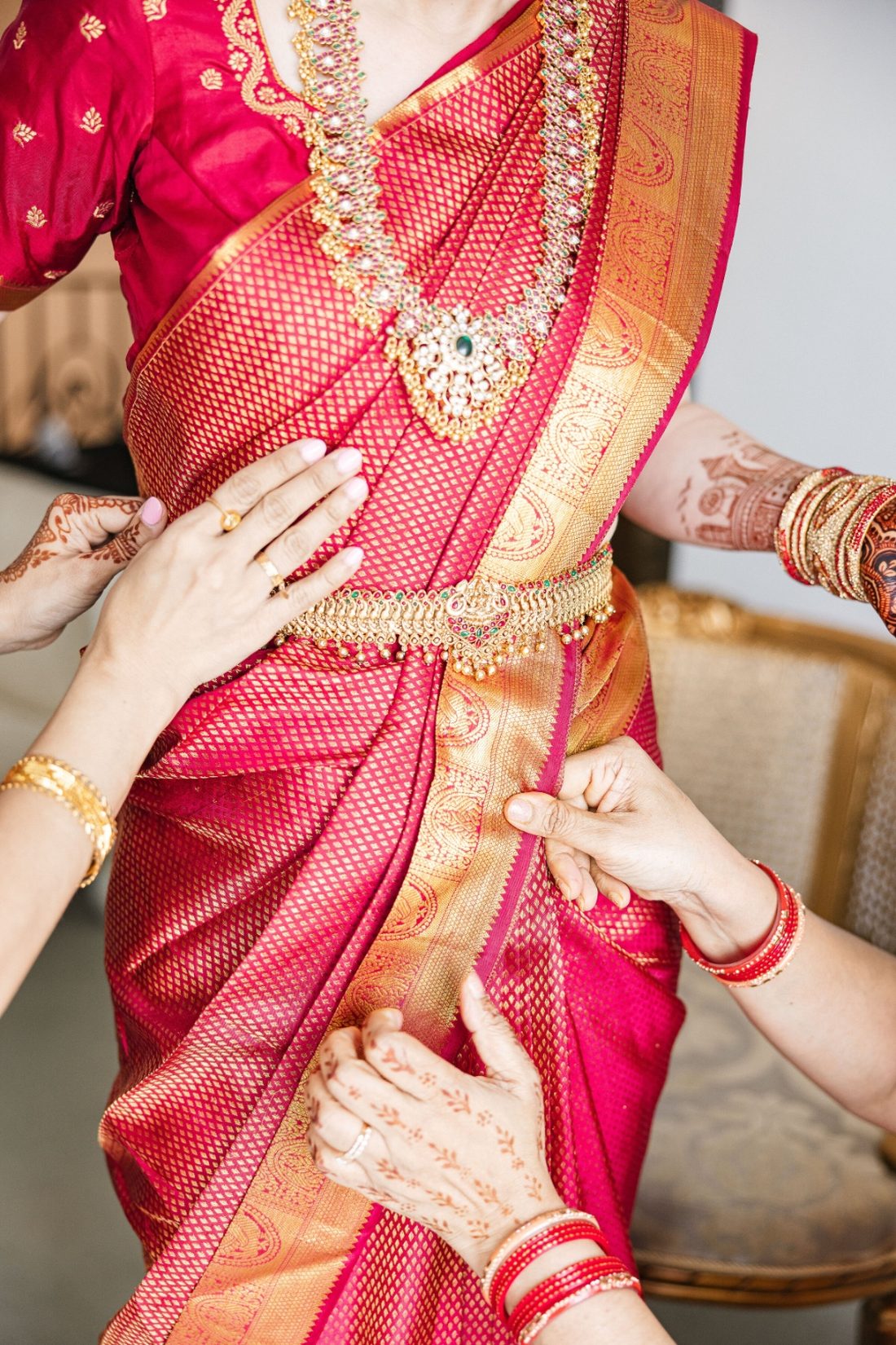Family hands draping a vibrant pink and gold Kanjeevaram saree on the bride